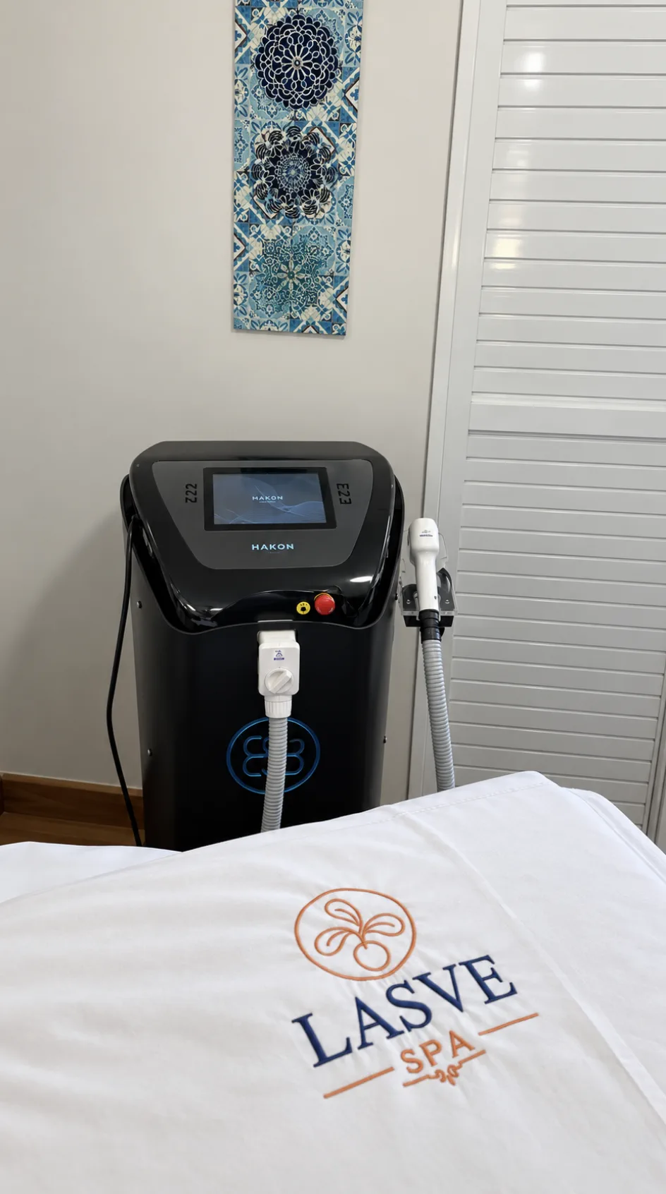 Equipamento de depilação a laser Hakon ao lado da maca com enxoval personalizado da LASVE